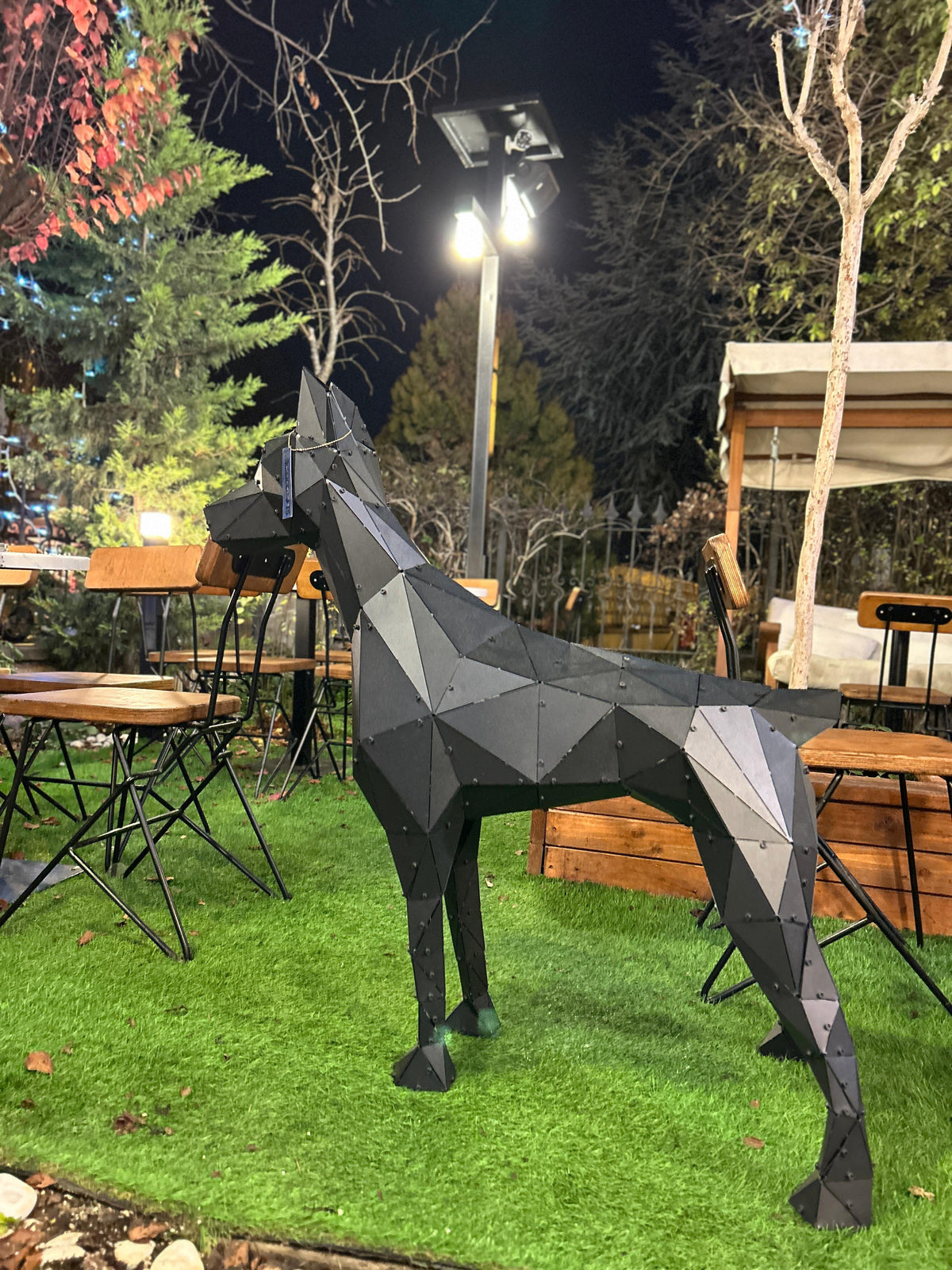 Geometric black metal dog sculpture on a green lawn at an outdoor restaurant setting