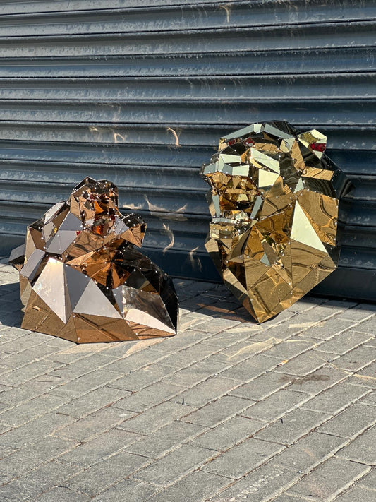 Gold mirrored geometric lion head and gorilla head sculptures on a paved street