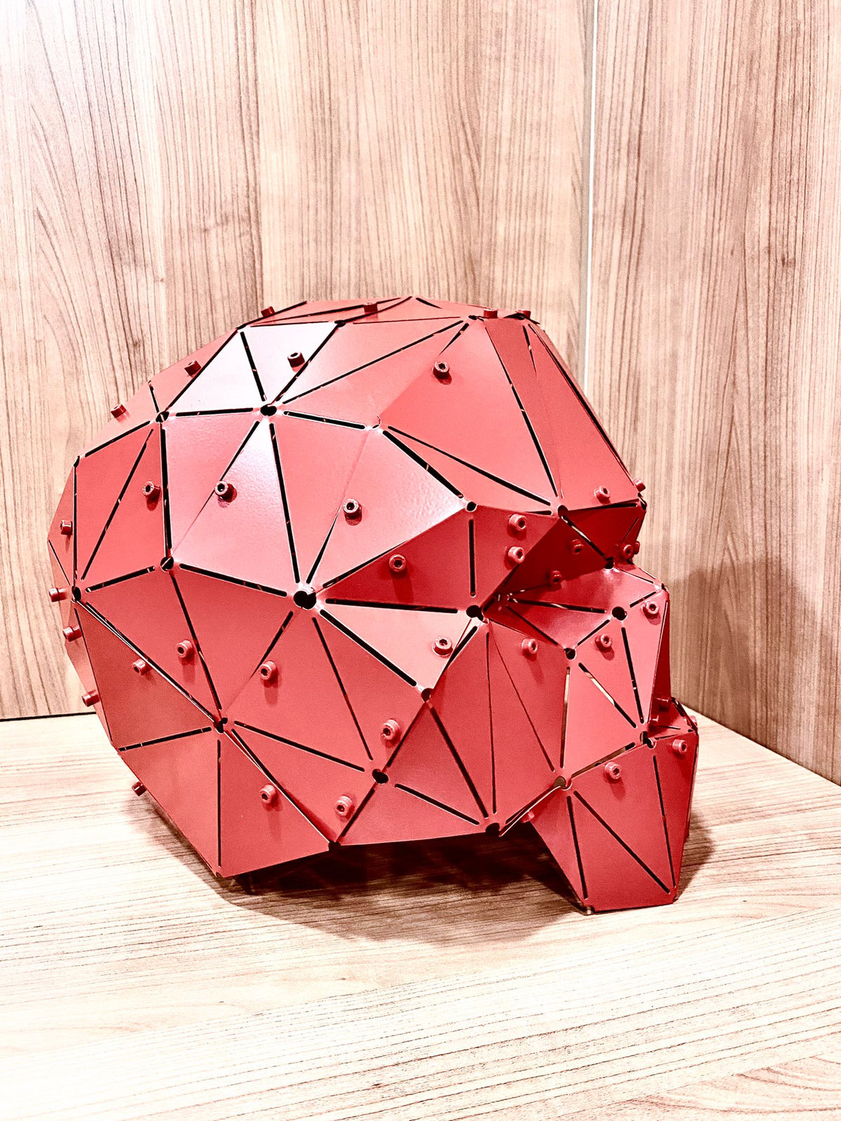 Handcrafted red geometric metal skull sculpture on a light wood surface, side view