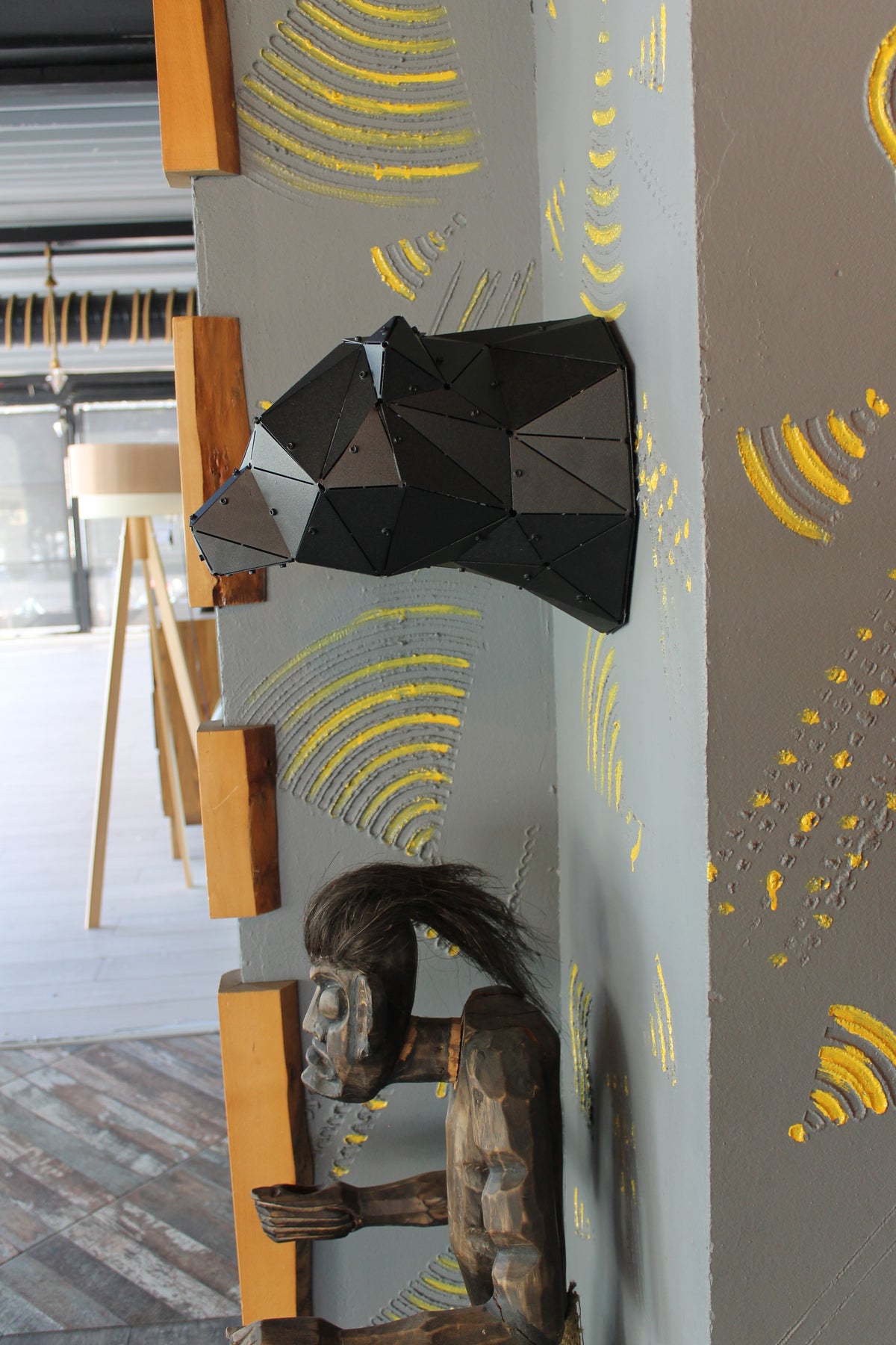 Low-poly black metal bear head wall sculpture on a grey textured wall with yellow accents