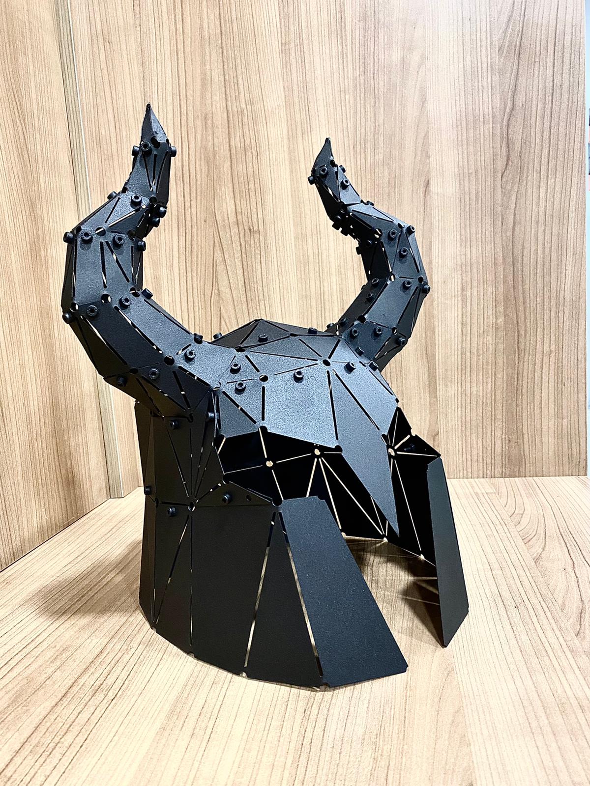 Low-poly black metal horned helmet sculpture, side angle on a wooden surface