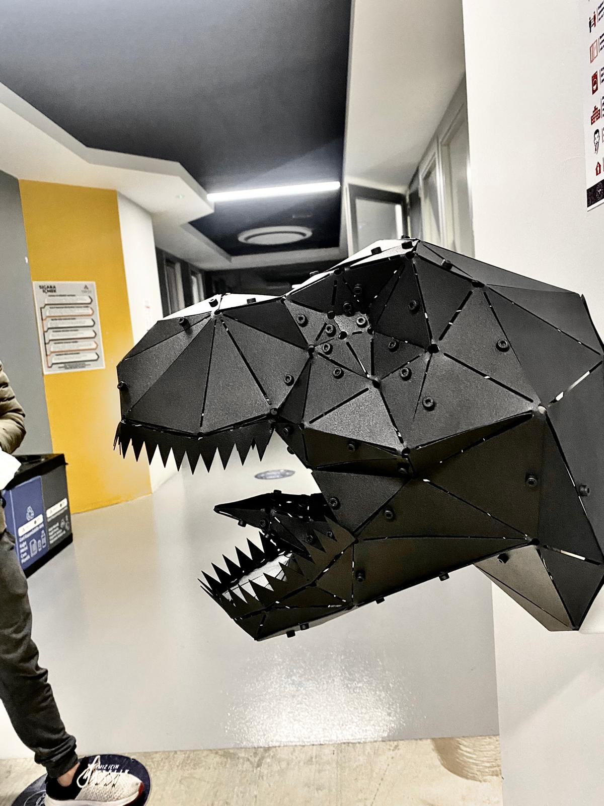 Modern black geometric metal dinosaur head sculpture mounted on a white wall.