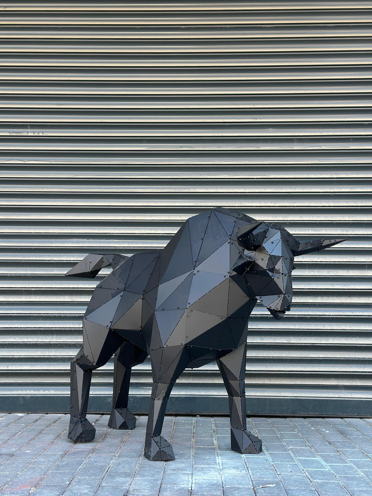 Modern geometric black metal bull sculpture against a corrugated metal background.