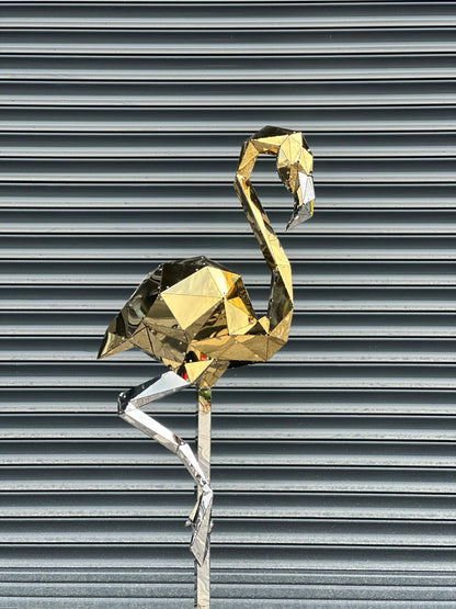Geometric gold and silver metal flamingo sculpture against a grey shutter background