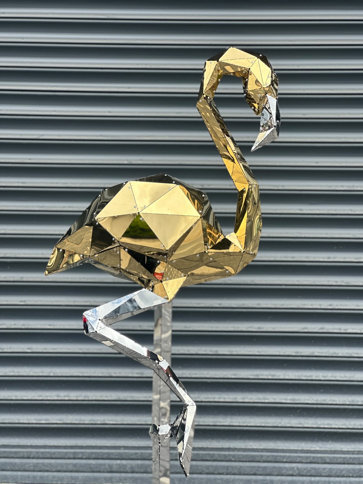 Luxury geometric gold and silver metal flamingo sculpture against a ribbed grey wall