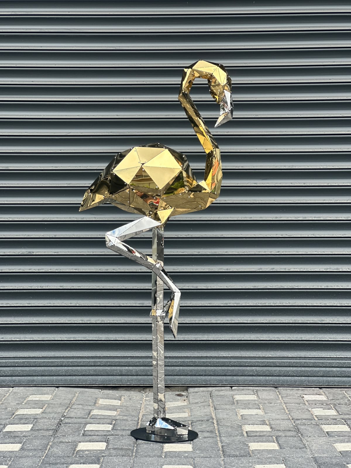 Low poly gold and silver metallic flamingo sculpture against a grey shutter background