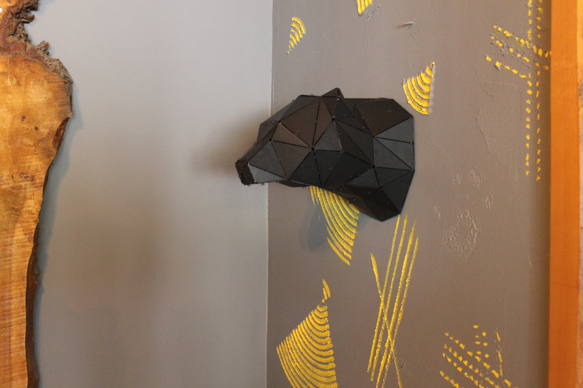 Black geometric low-poly bear head wall sculpture on a grey wall with yellow accents