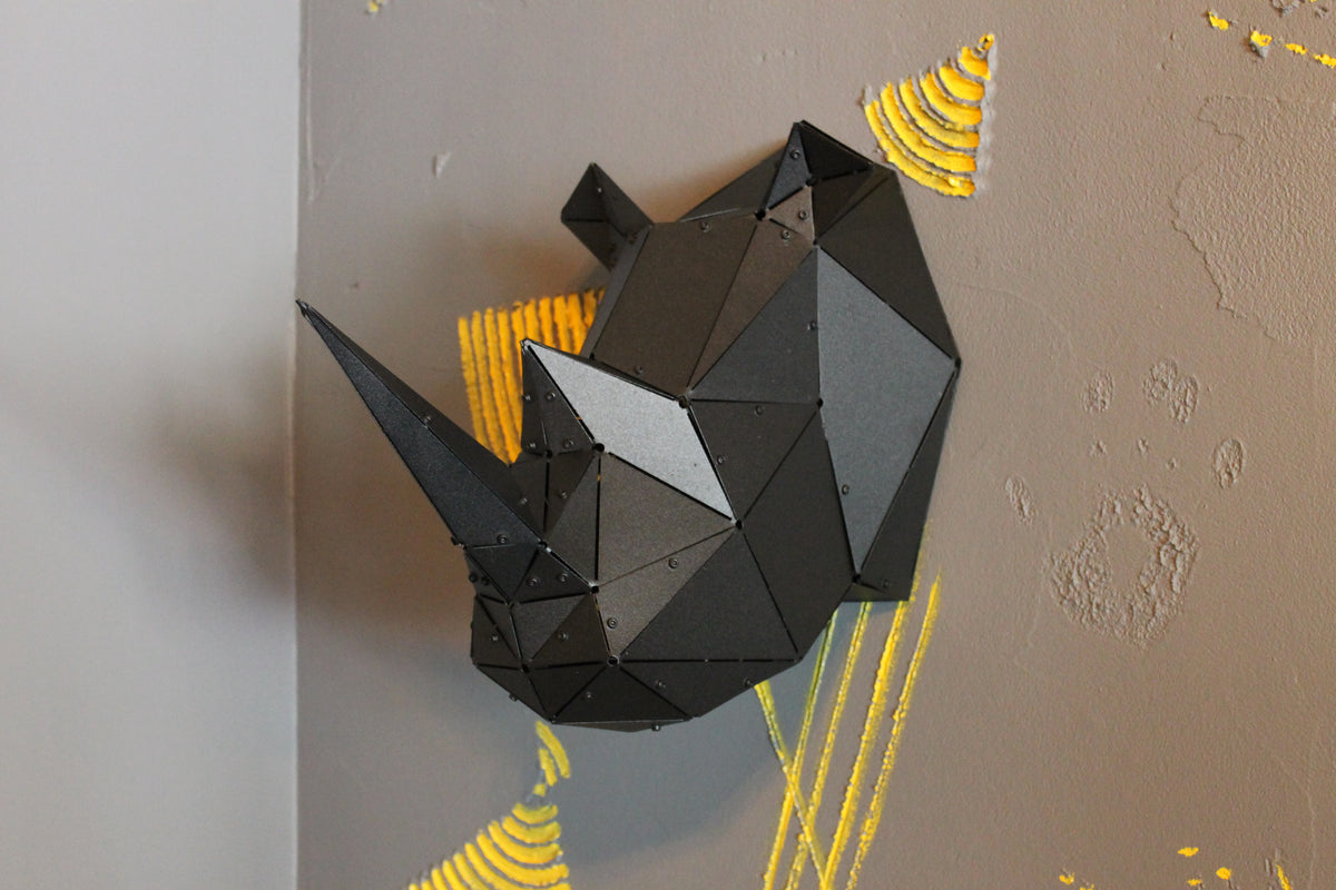 Black geometric metal rhino head sculpture mounted on a grey wall with yellow accents