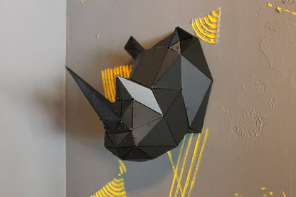Black geometric metal rhino head sculpture mounted on a grey wall with yellow accents