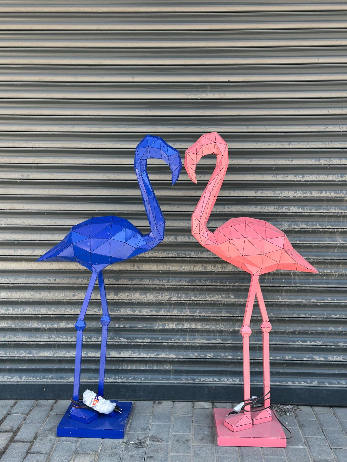Two geometric metal flamingo sculptures, one blue and one pink, facing each other.