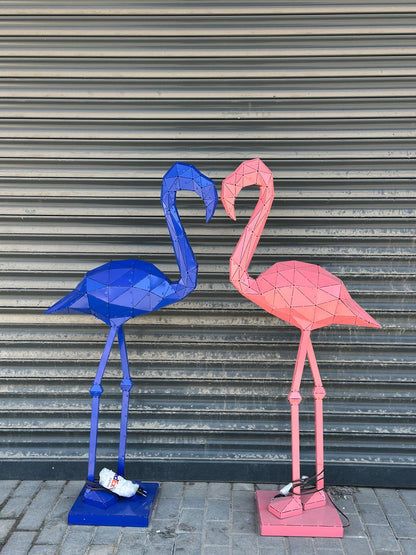 Two geometric metal flamingo sculptures, one blue and one pink, facing each other.