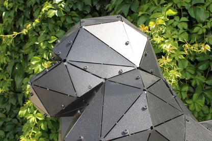 Close-up of a handcrafted geometric metal gorilla sculpture against lush green foliage.