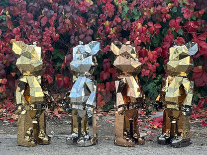 Four geometric faceted metal bear sculptures in gold and silver against autumn foliage.