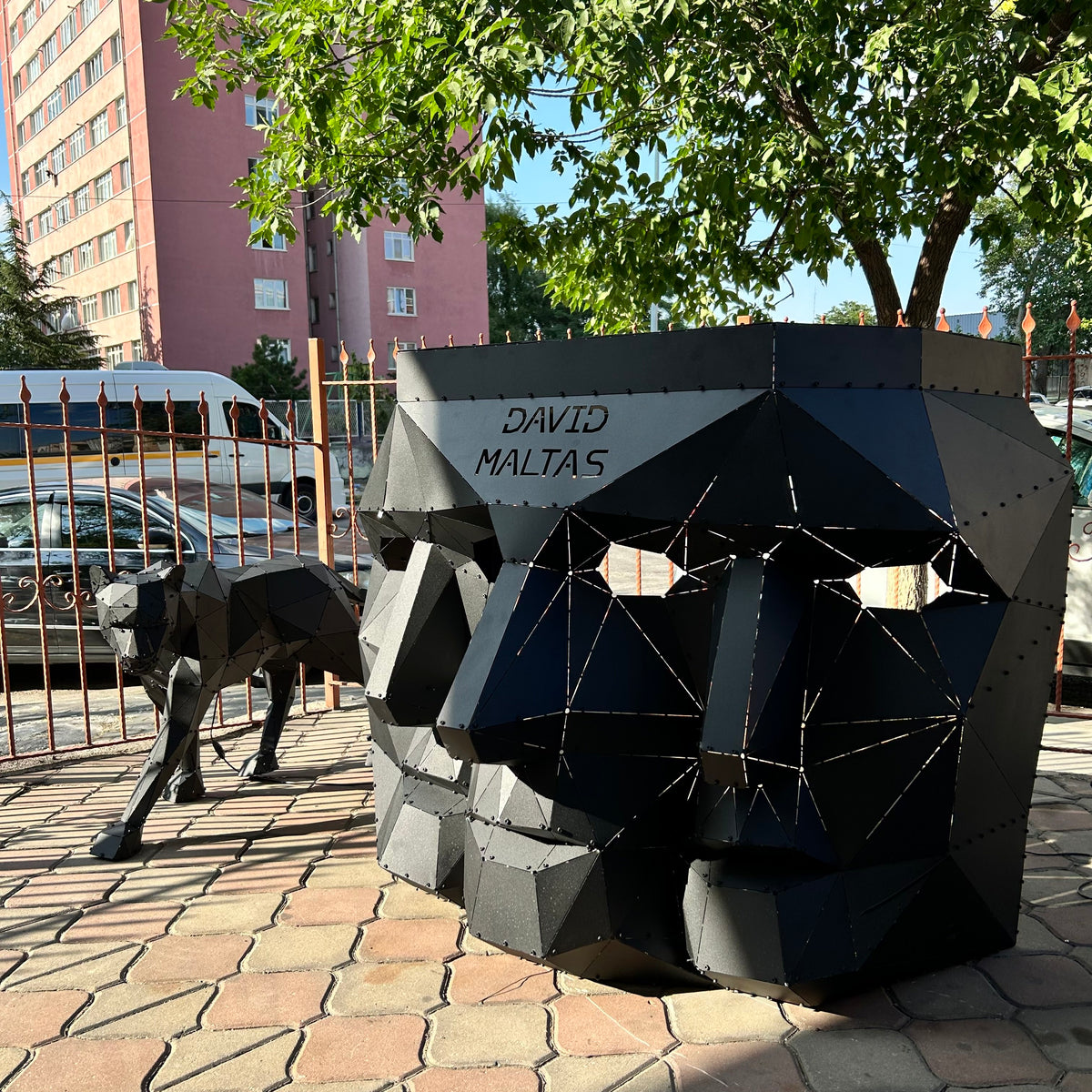 Geometric black metal sculptures of a face and a wolf by David Maltas outdoors.