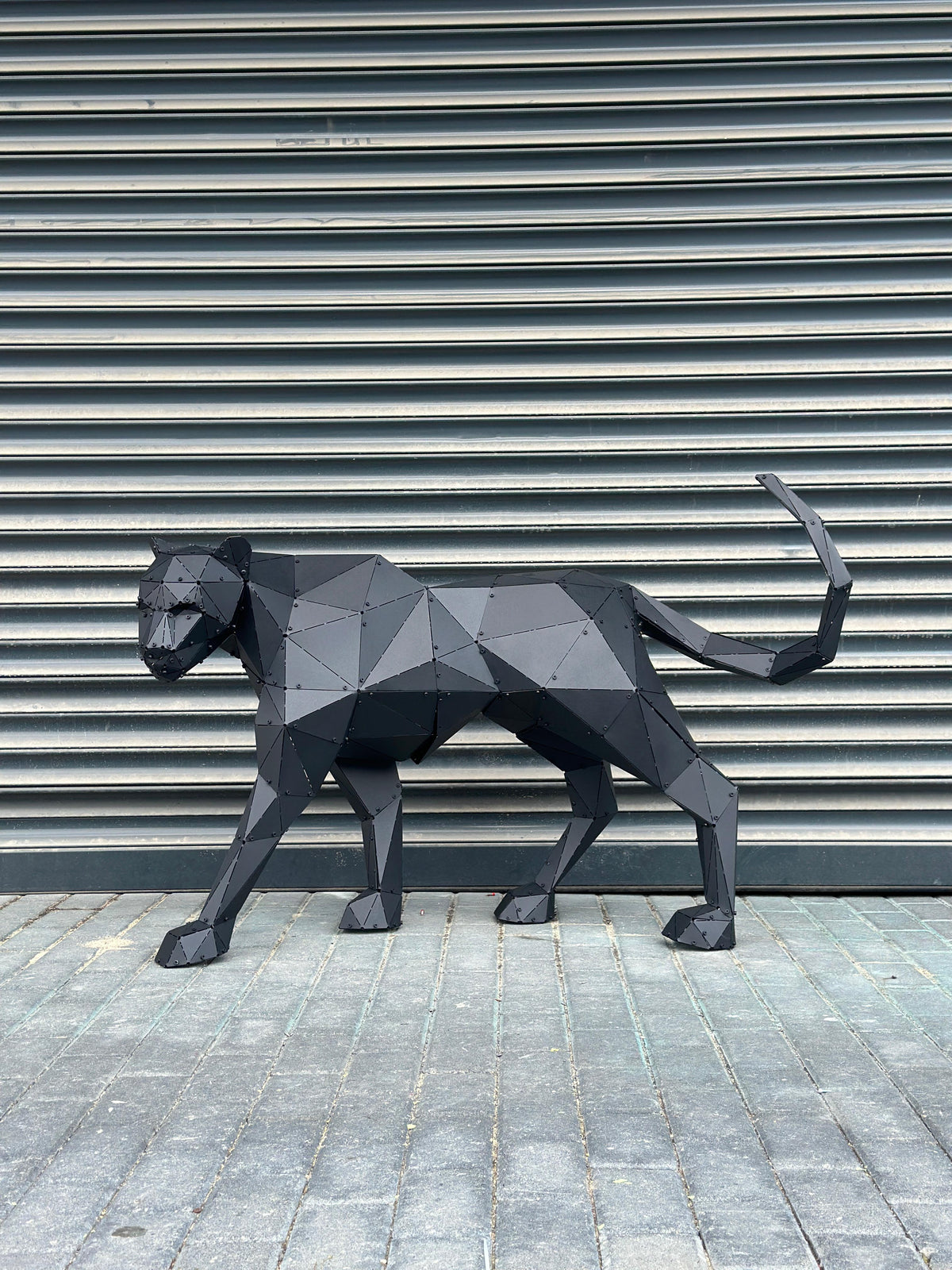 Geometric black metal panther sculpture standing against a grey shutter background.