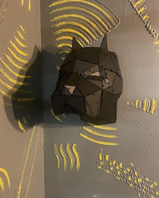 Geometric black metal pitbull head sculpture mounted on a grey textured wall with yellow accents