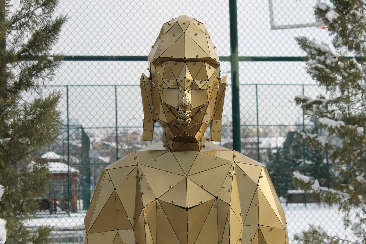 Close-up of gold geometric metal Buddha sculpture head and shoulders in snow