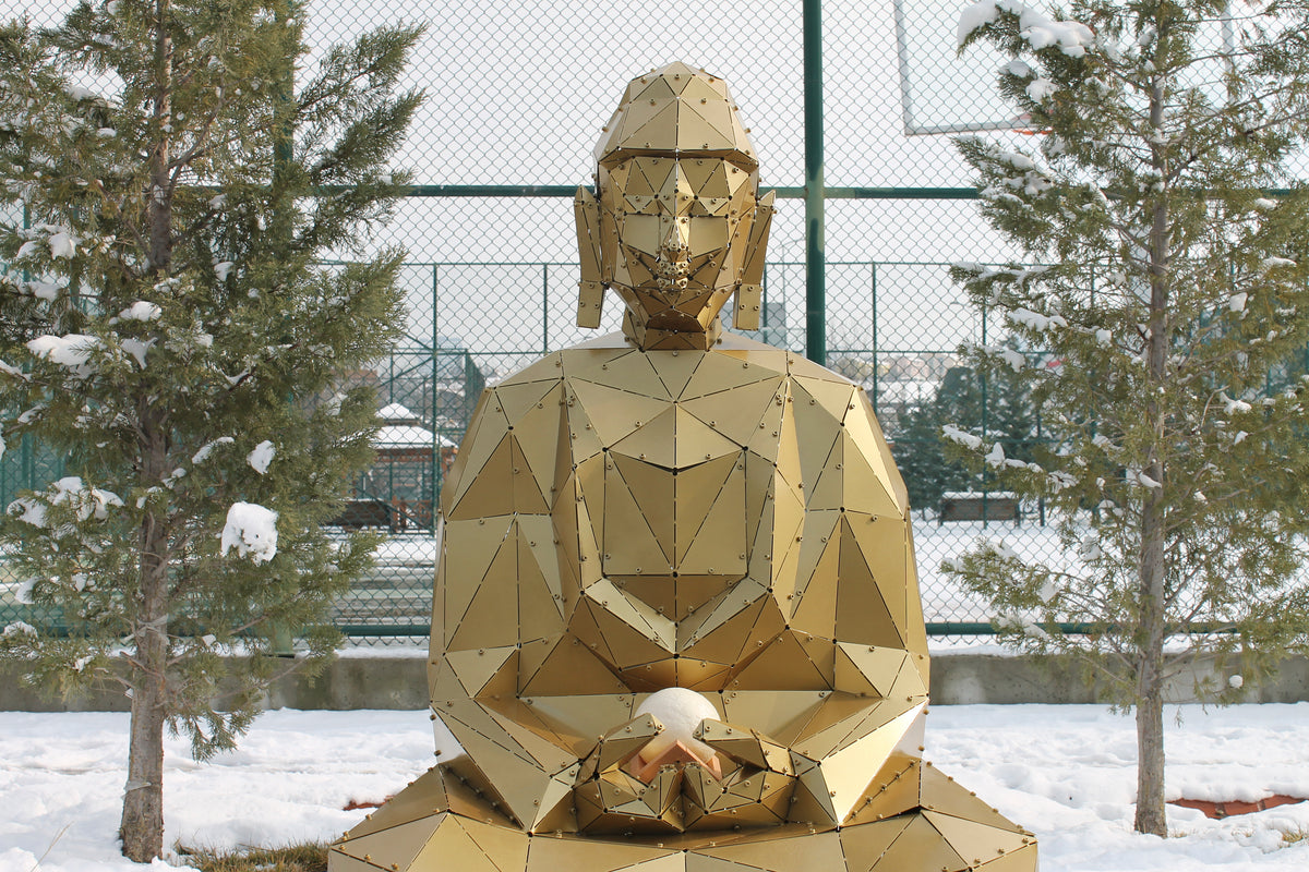 Geometric gold metal Buddha sculpture meditating in a snowy outdoor setting