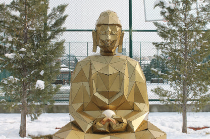 Geometric gold metal Buddha sculpture meditating in a snowy outdoor setting