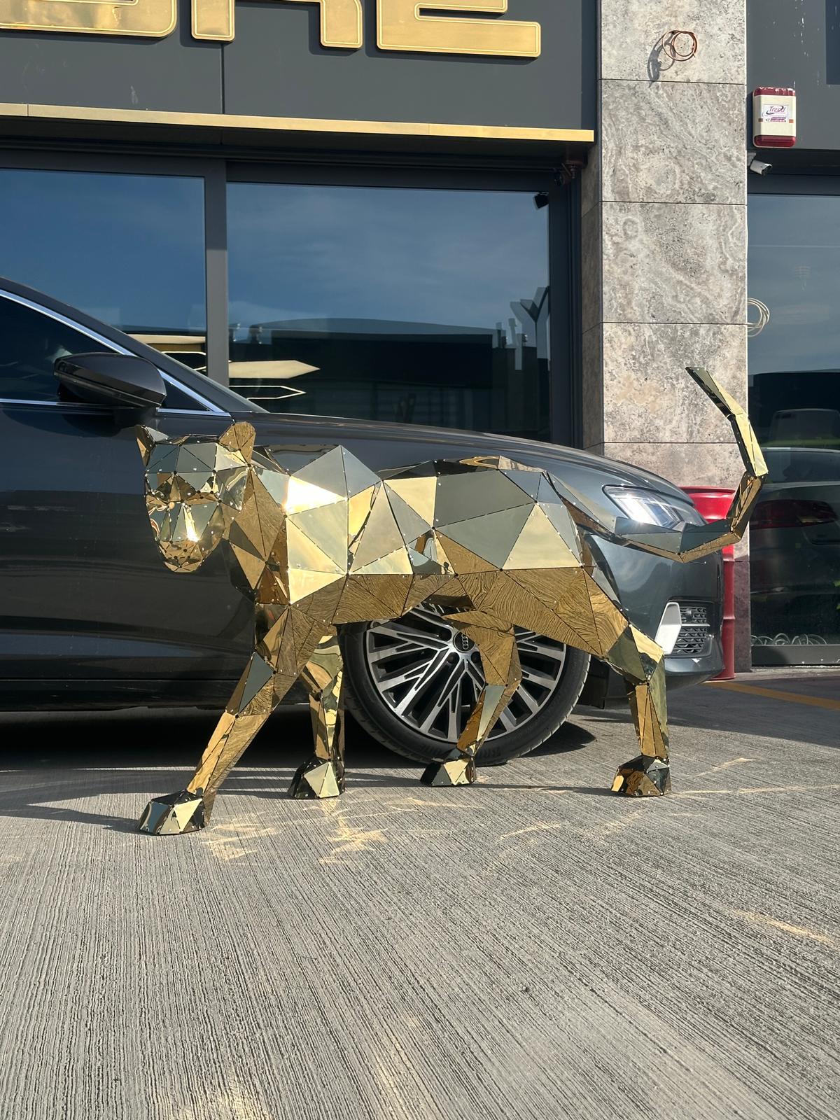 Geometric gold metal panther sculpture standing beside a luxury car