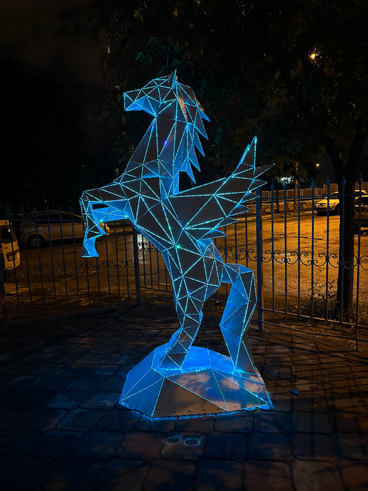 Geometric low-poly Pegasus metal sculpture with glowing blue LED lighting at night