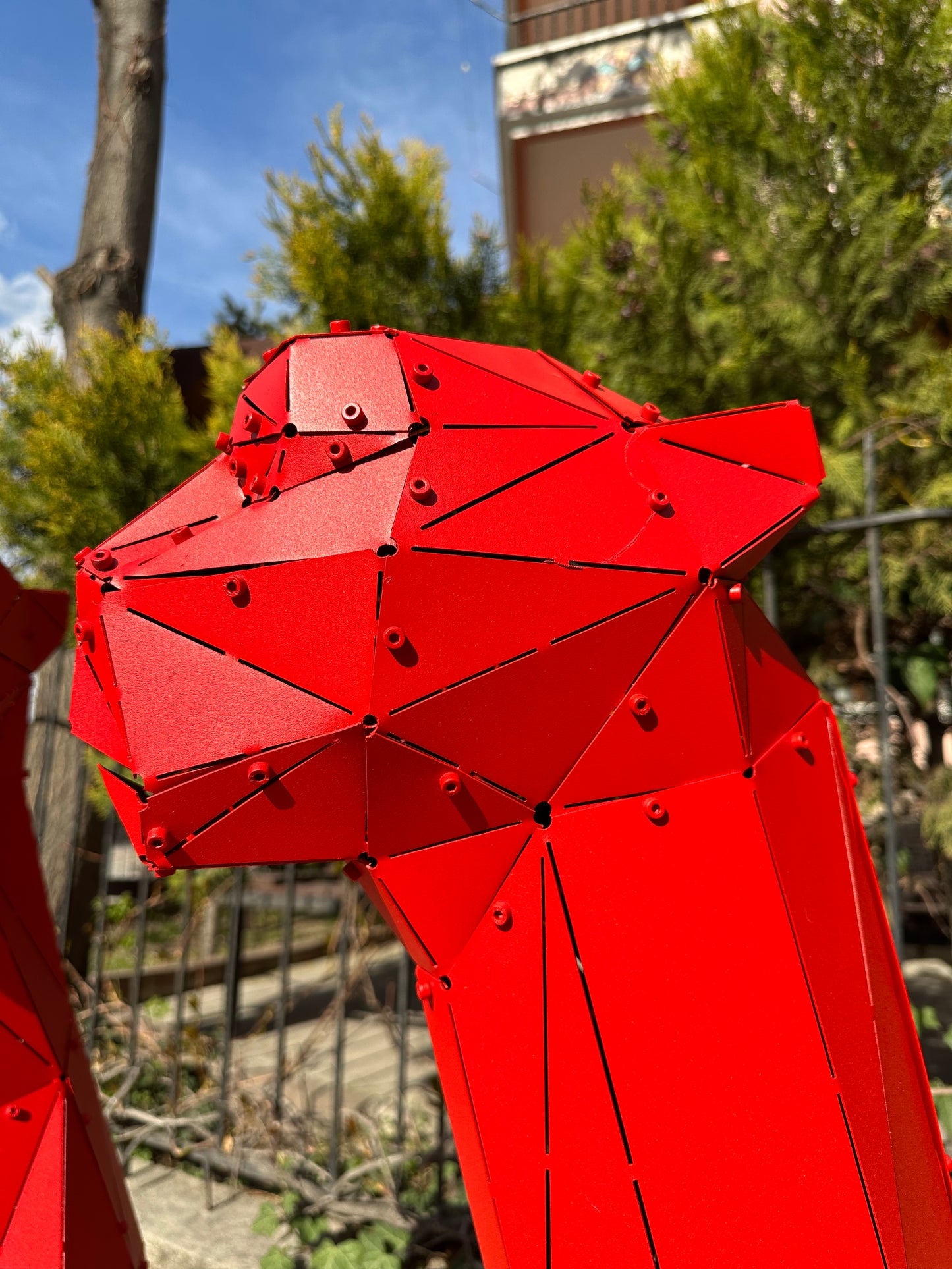 Close-up of a red geometric metal big cat head sculpture outdoors