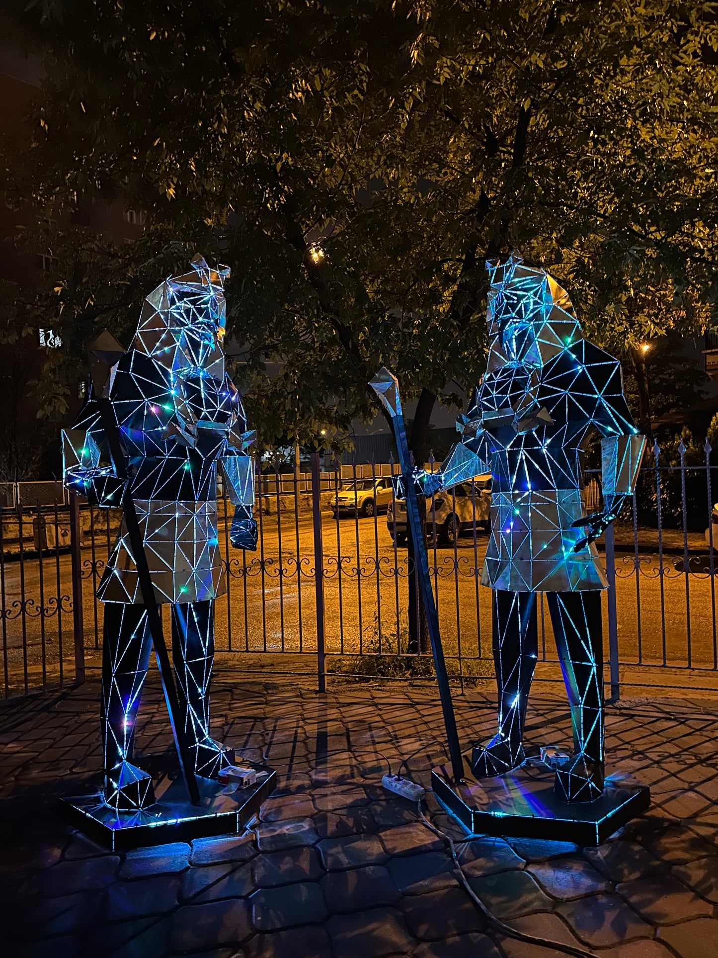 Two geometric metal Egyptian pharaoh sculptures lit with blue light outdoors at night
