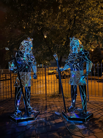 Two geometric metal Egyptian pharaoh sculptures lit with blue light outdoors at night