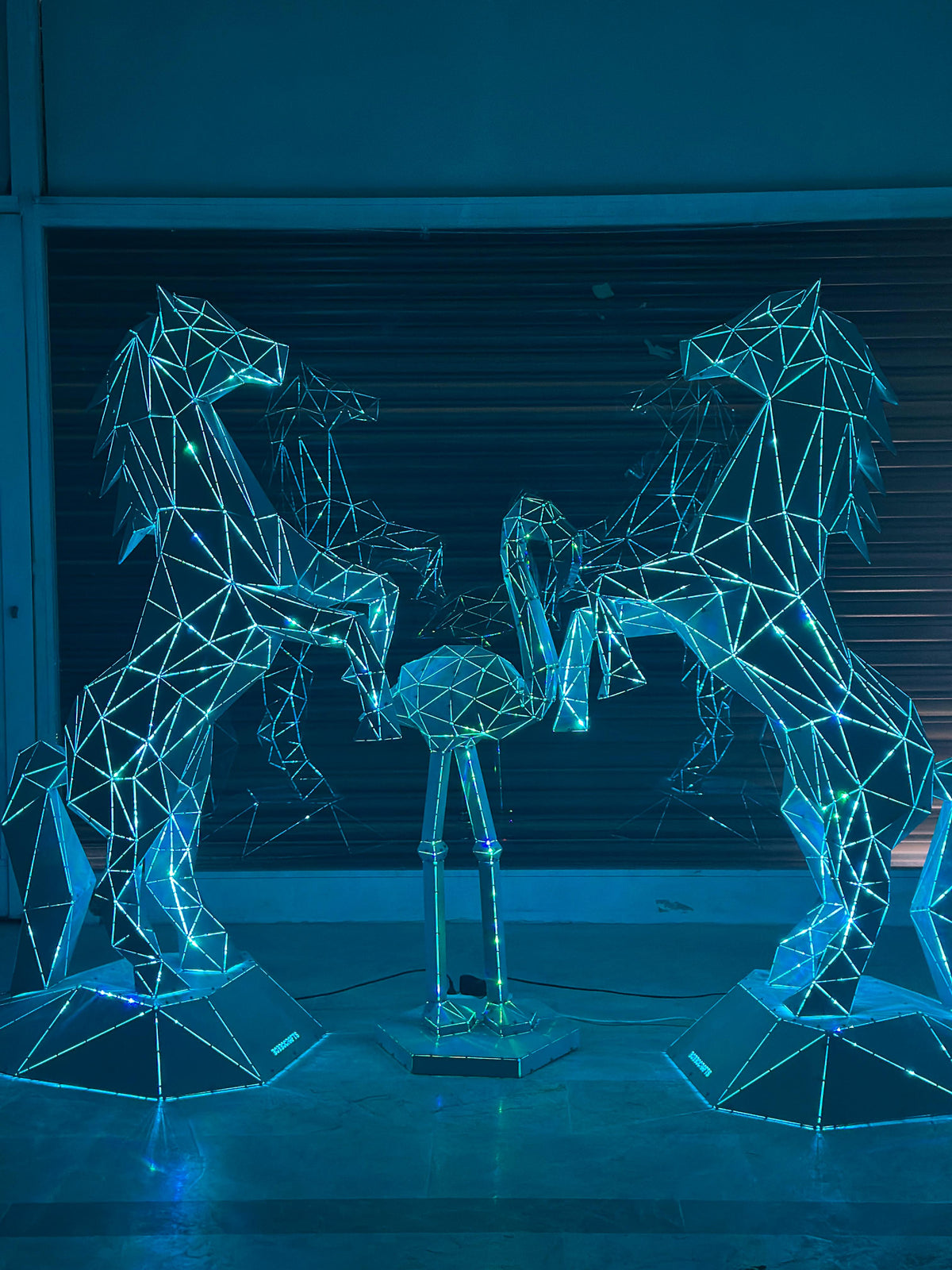 Geometric metal sculptures of horses and a bird illuminated with blue lights