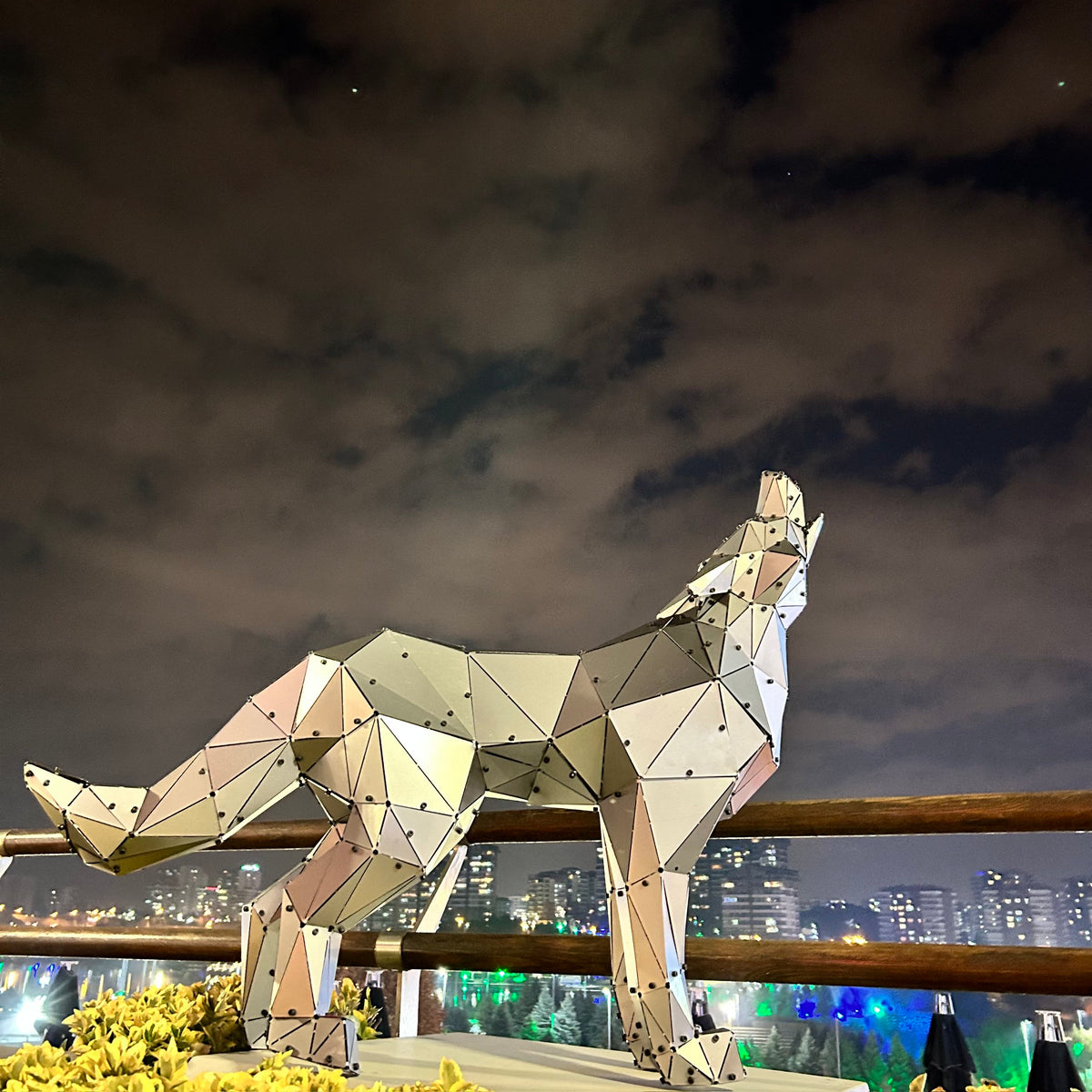 Geometric metal wolf sculpture on a balcony against a dramatic night sky.