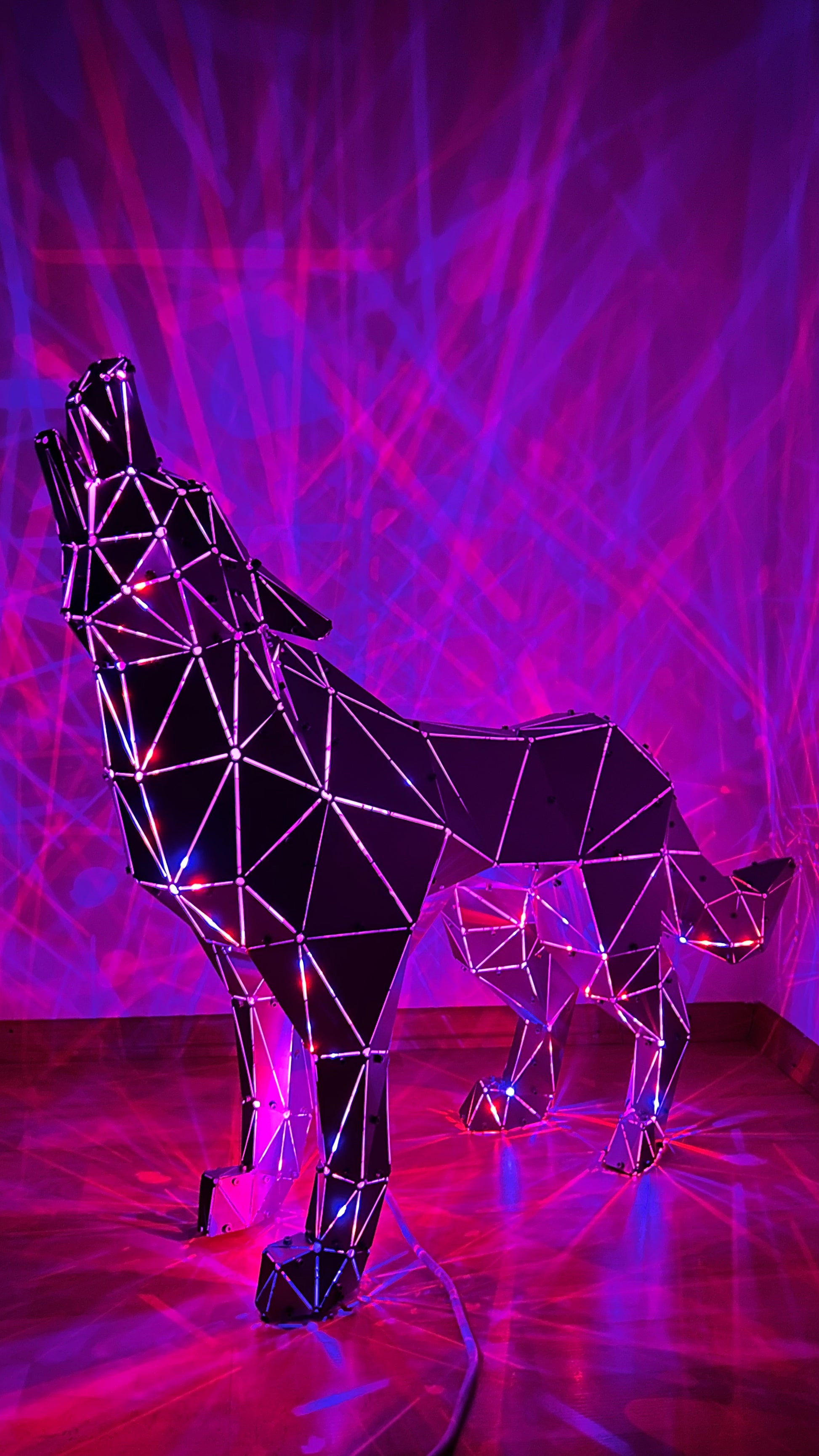 Geometric metal wolf sculpture howling against a purple laser light backdrop