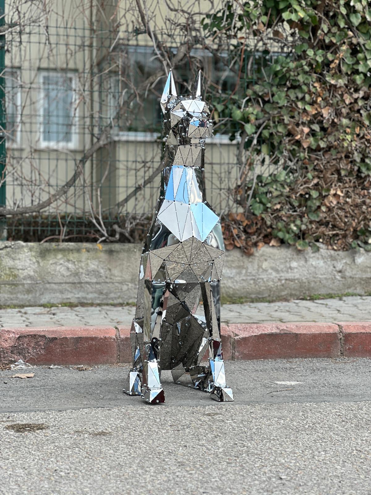 Geometric mirrored metal sculpture of a sitting dog on a city sidewalk
