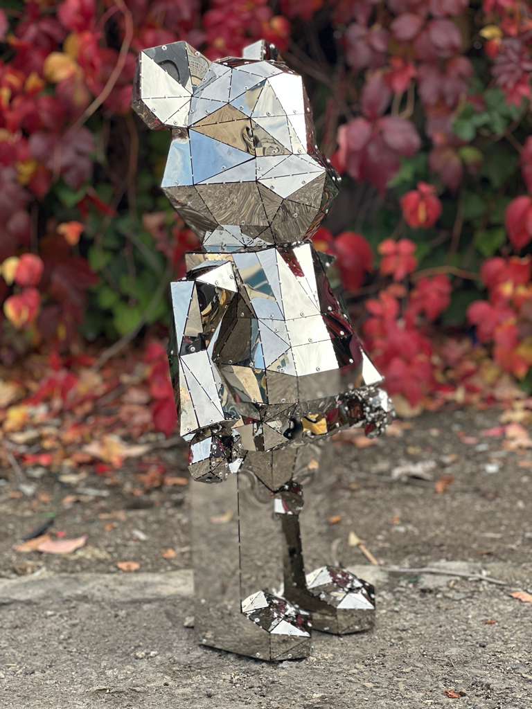 Geometric polished mirror metal bear sculpture against a backdrop of red autumn leaves.