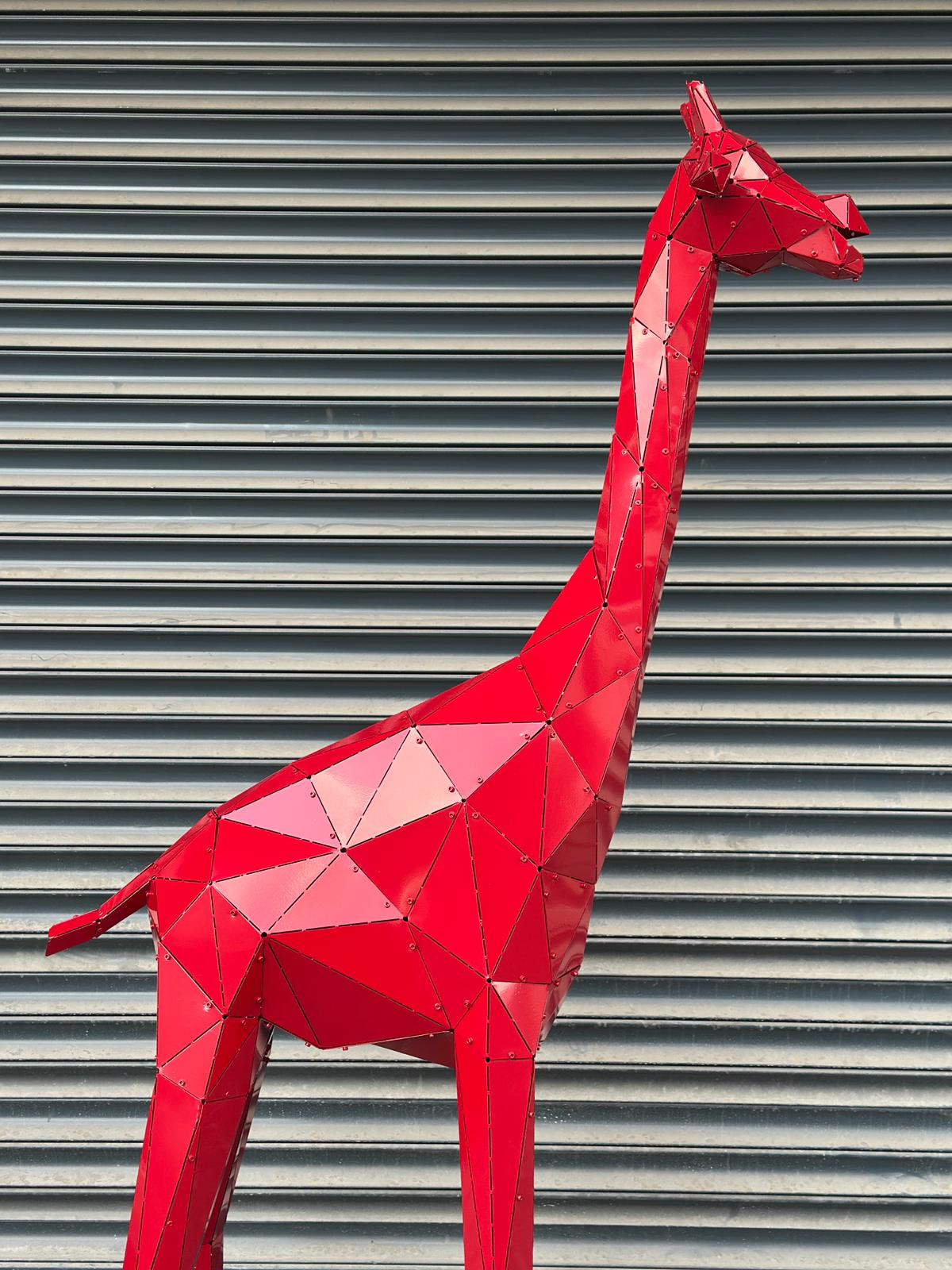 Geometric red metal giraffe sculpture against a grey corrugated background
