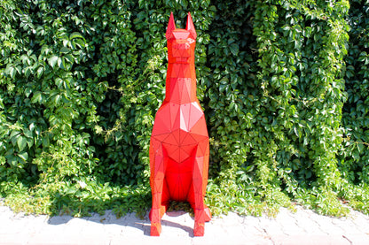Geometric red metal Doberman sculpture sitting against a lush green ivy wall