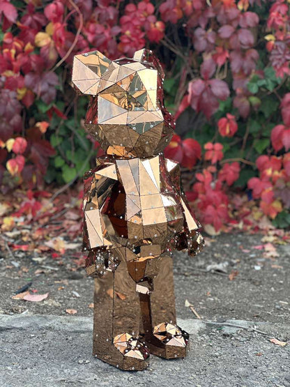 Geometric rose gold polished metal bear sculpture against autumn foliage