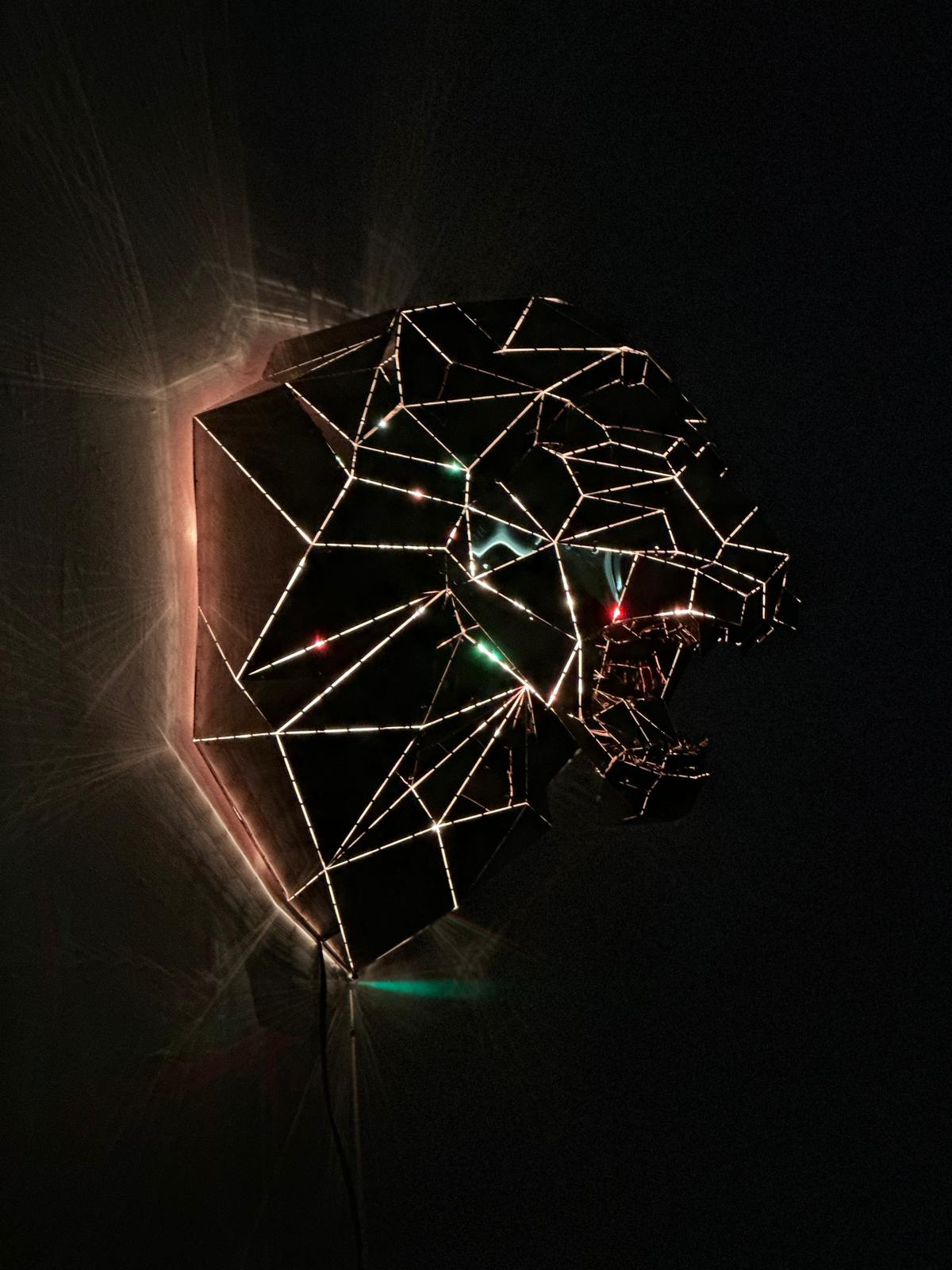 Geometric wireframe sculpture of a lion's head with integrated LED lighting against a dark background