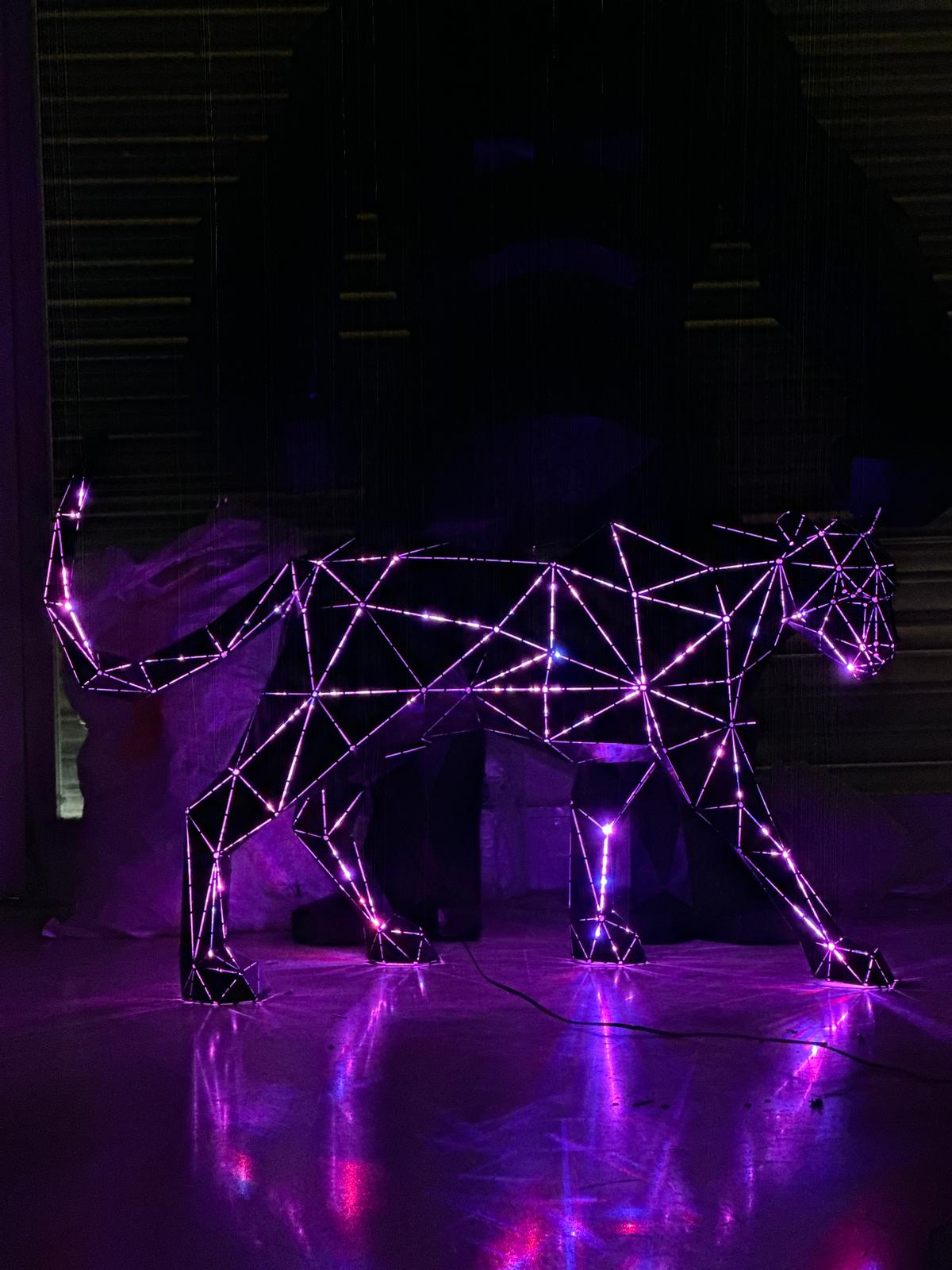 Glowing purple geometric metal sculpture of a prowling panther with LED lighting