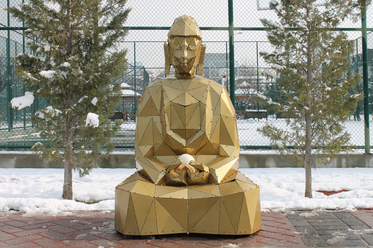 Gold geometric metal Buddha sculpture in a meditative pose outdoors in a snowy landscape