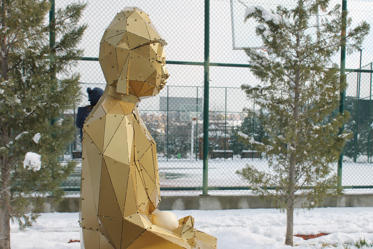Side view of gold geometric metal Buddha sculpture in a snowy outdoor court