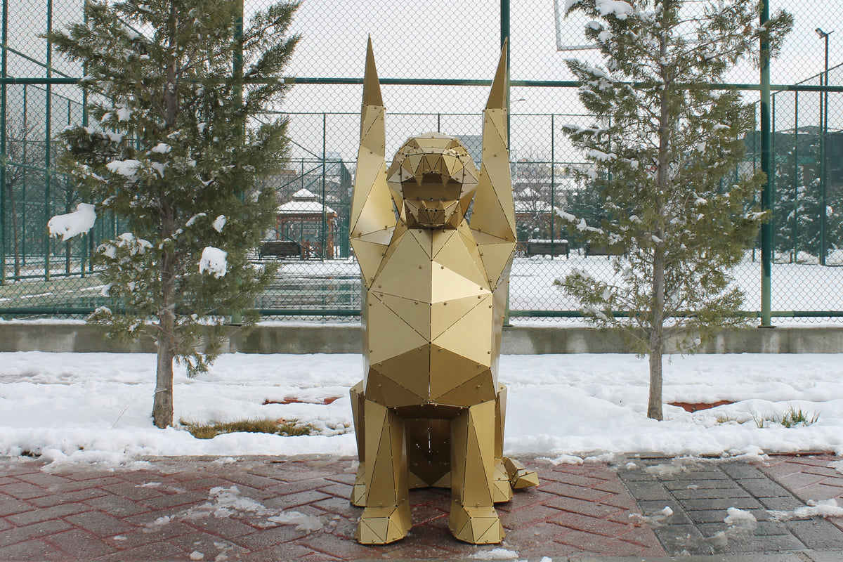 Gold geometric metal griffin sculpture seated with raised wings in a snowy outdoor setting