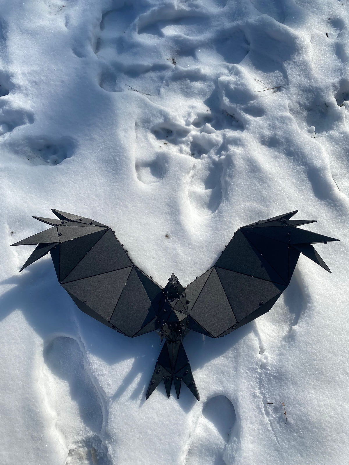 Handcrafted black geometric metal bird sculpture resting on white snow.