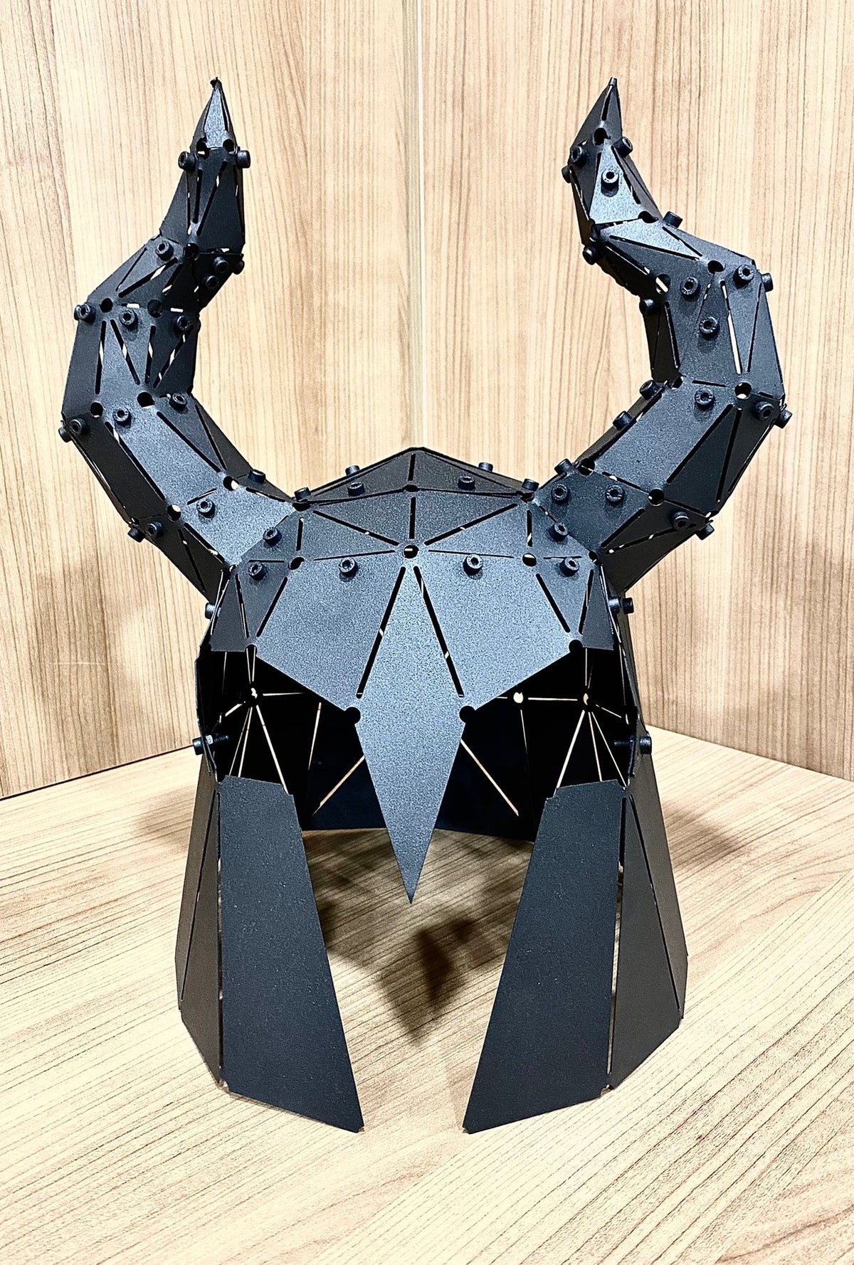 Handcrafted black metal low-poly horned helmet sculpture on a wooden surface.