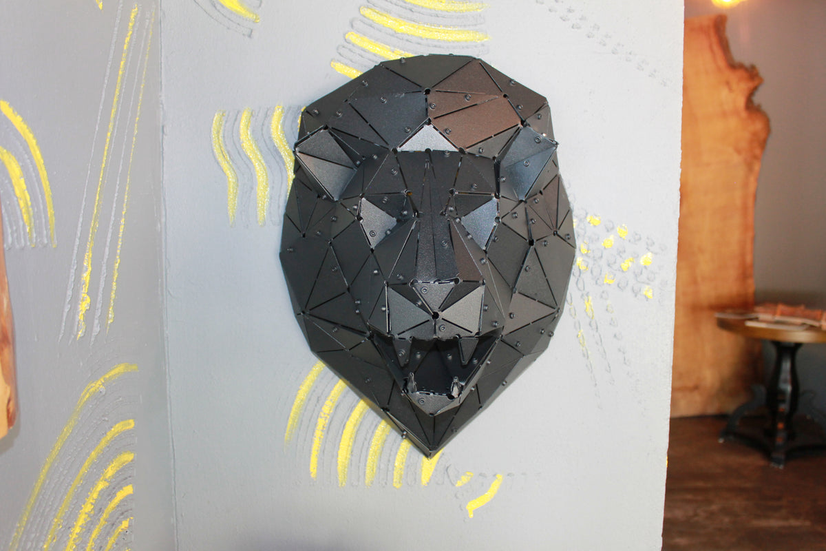 Handcrafted black metal low-poly lion head sculpture mounted on a gray textured wall