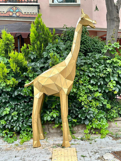 Handcrafted gold geometric metal giraffe sculpture standing amidst lush green foliage