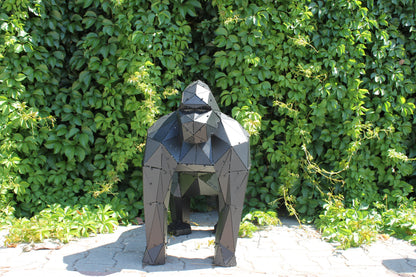 Handcrafted low-poly metal gorilla sculpture positioned against a lush green hedge background