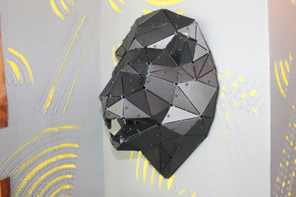 Handcrafted low-poly black metal lion head wall sculpture in profile on a textured grey wall