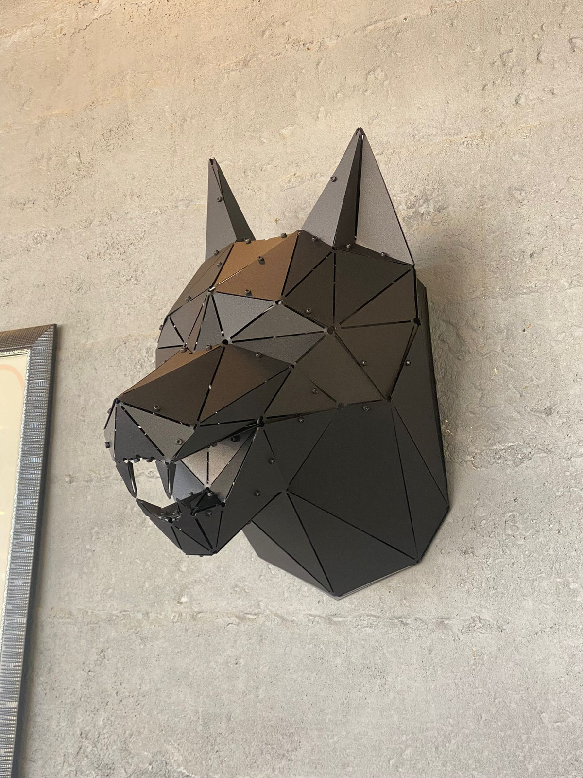 Handcrafted low-poly metal wolf head sculpture mounted on a grey concrete wall