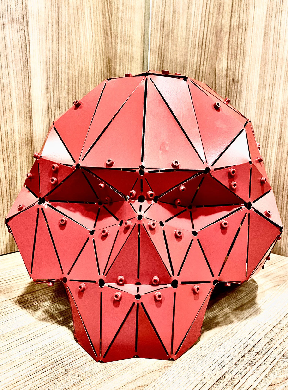 Handcrafted red geometric metal skull sculpture on a wooden surface