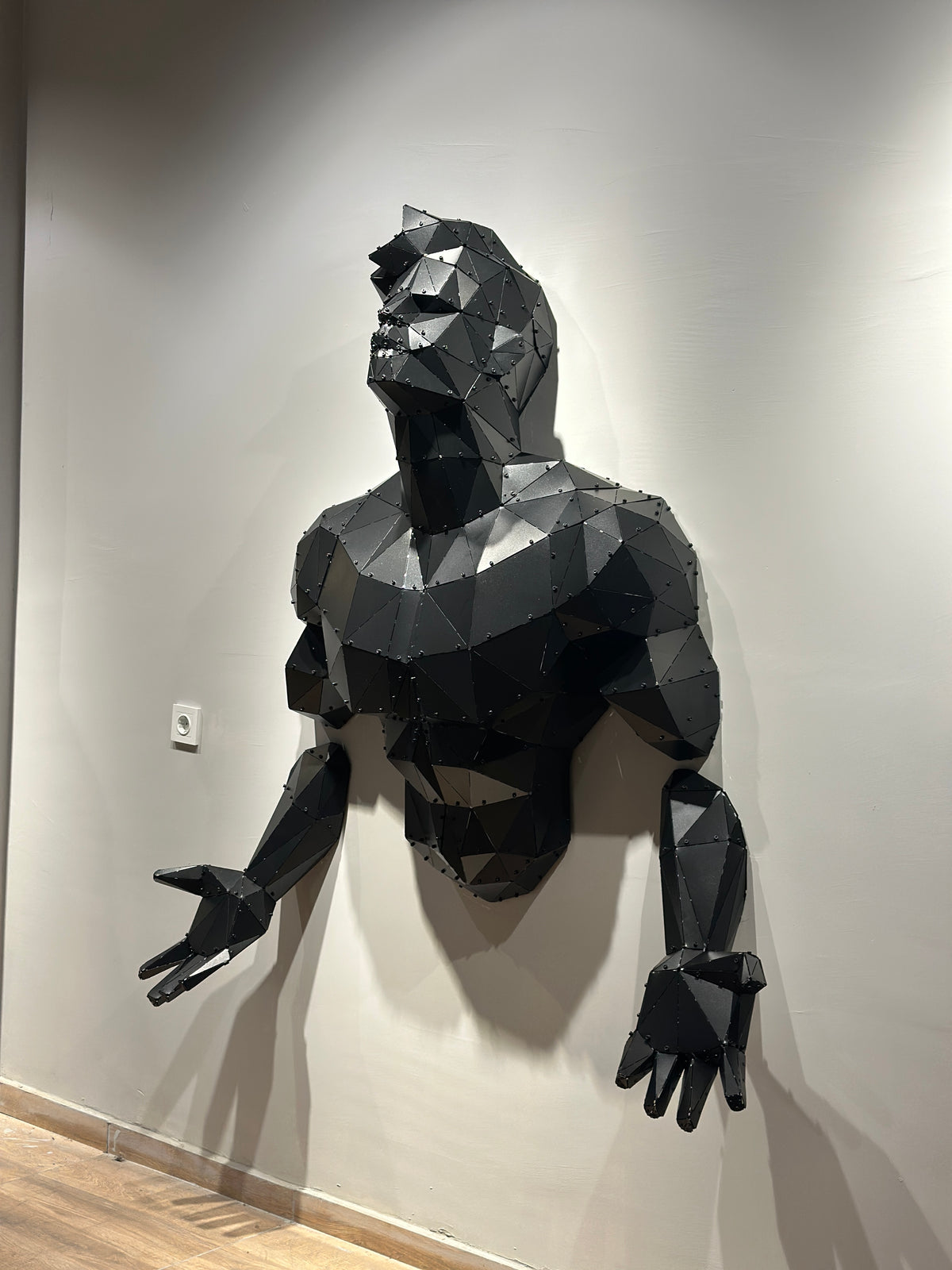 Industrial matte black low-poly metal man wall sculpture emerging from a white wall